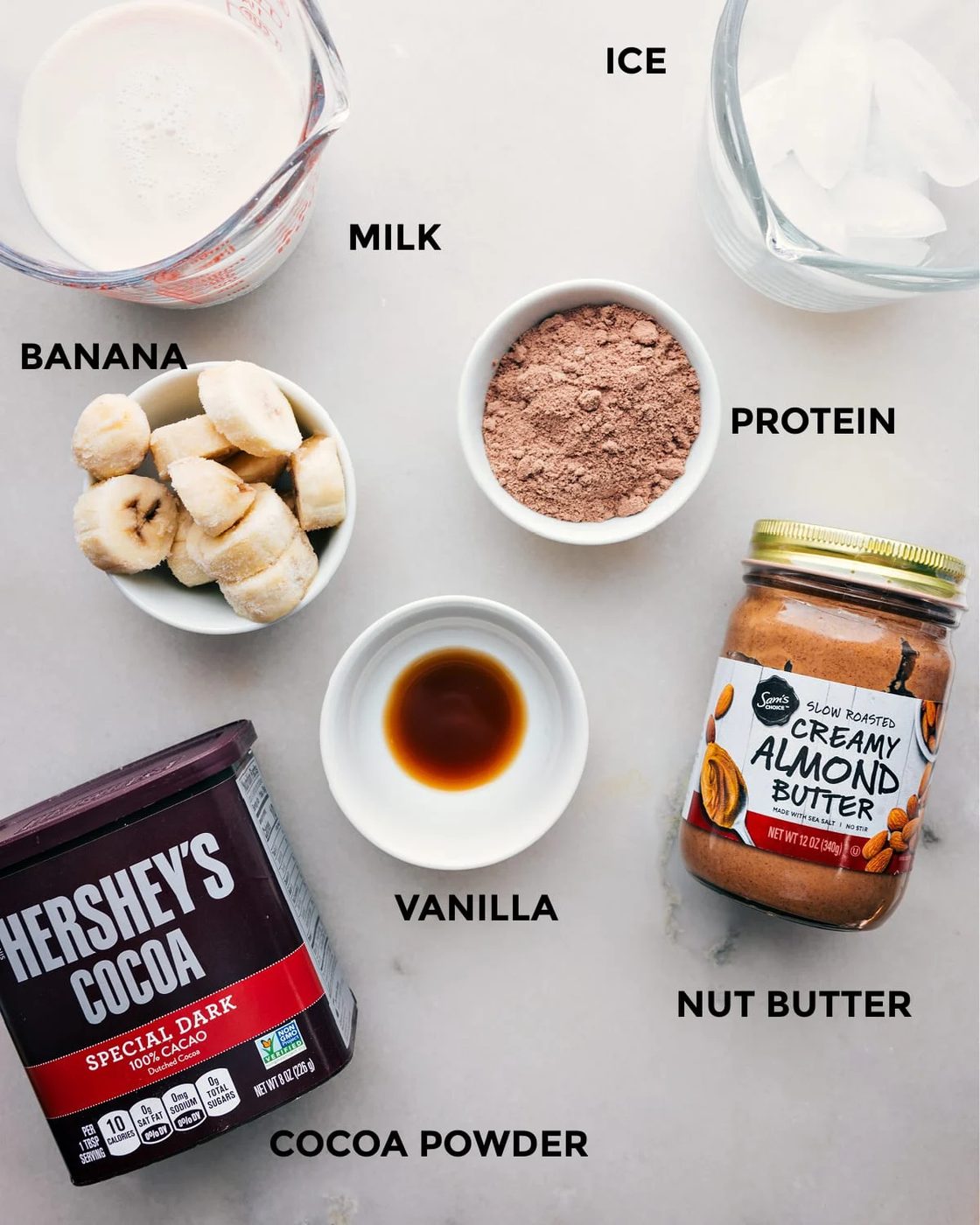 All the ingredients including milk, ice, cocoa powder, nut butter, vanilla, and protein powder prepped out for straightforward assembly.