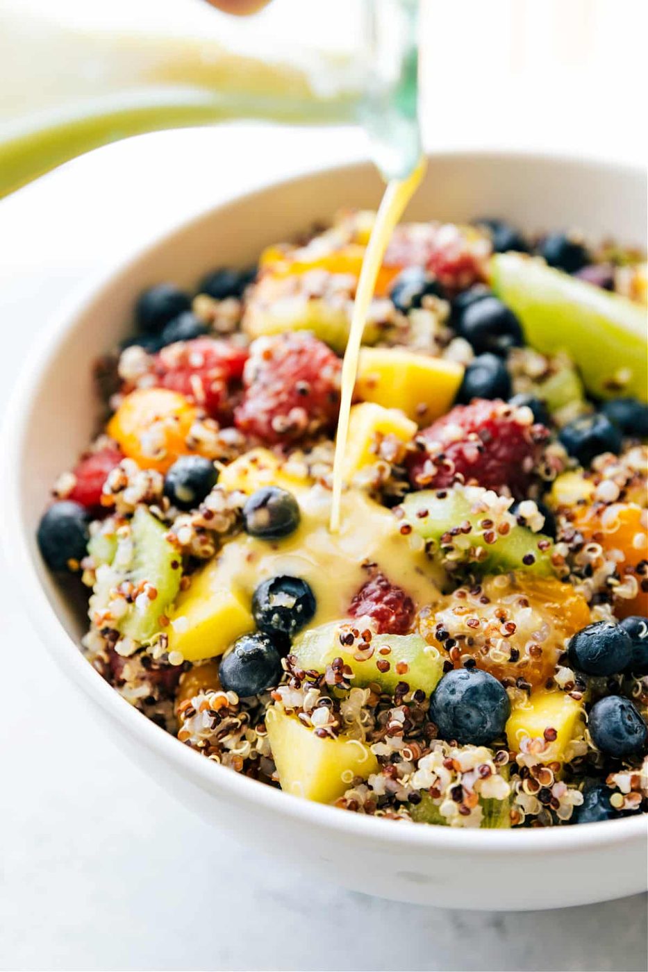 Quinoa Fruit Salad with the dressing being poured over it.