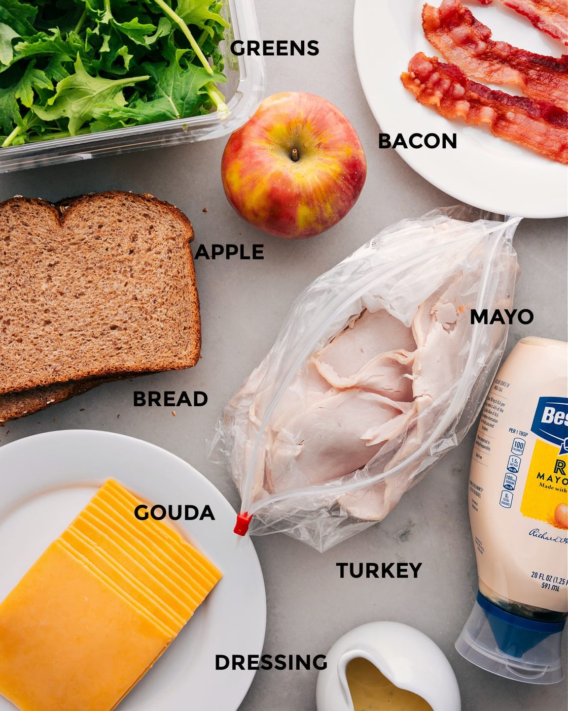 All the ingredients in this recipe, including the meats, apple, greens, bread, cheese, mayo, and dressing, are prepped for straightforward assembly.