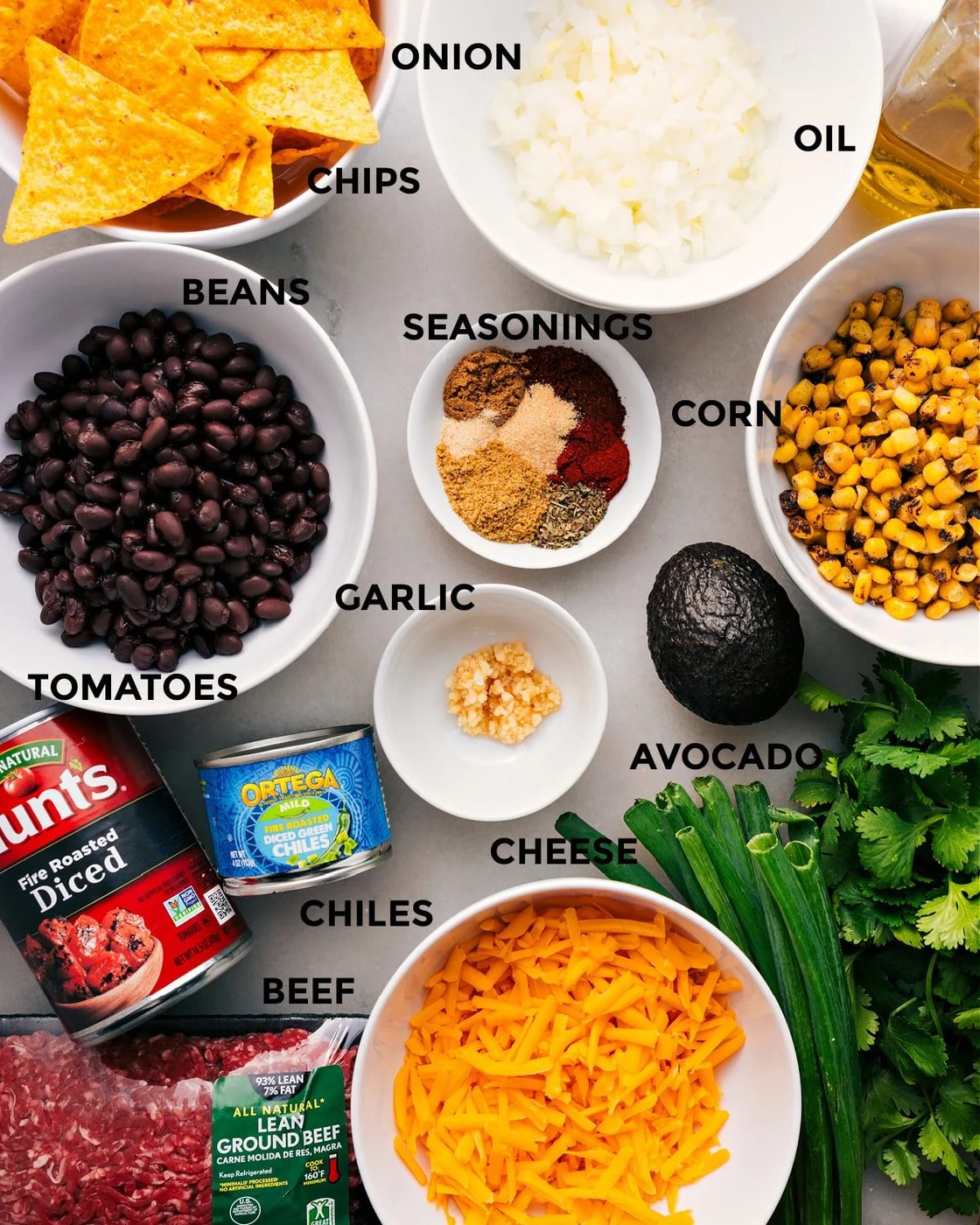 Prep all the ingredients for straightforward assembly, including the seasonings, meat, corn, avocado, garlic, tomatoes, chiles, cheese, chips, and fresh herbs.