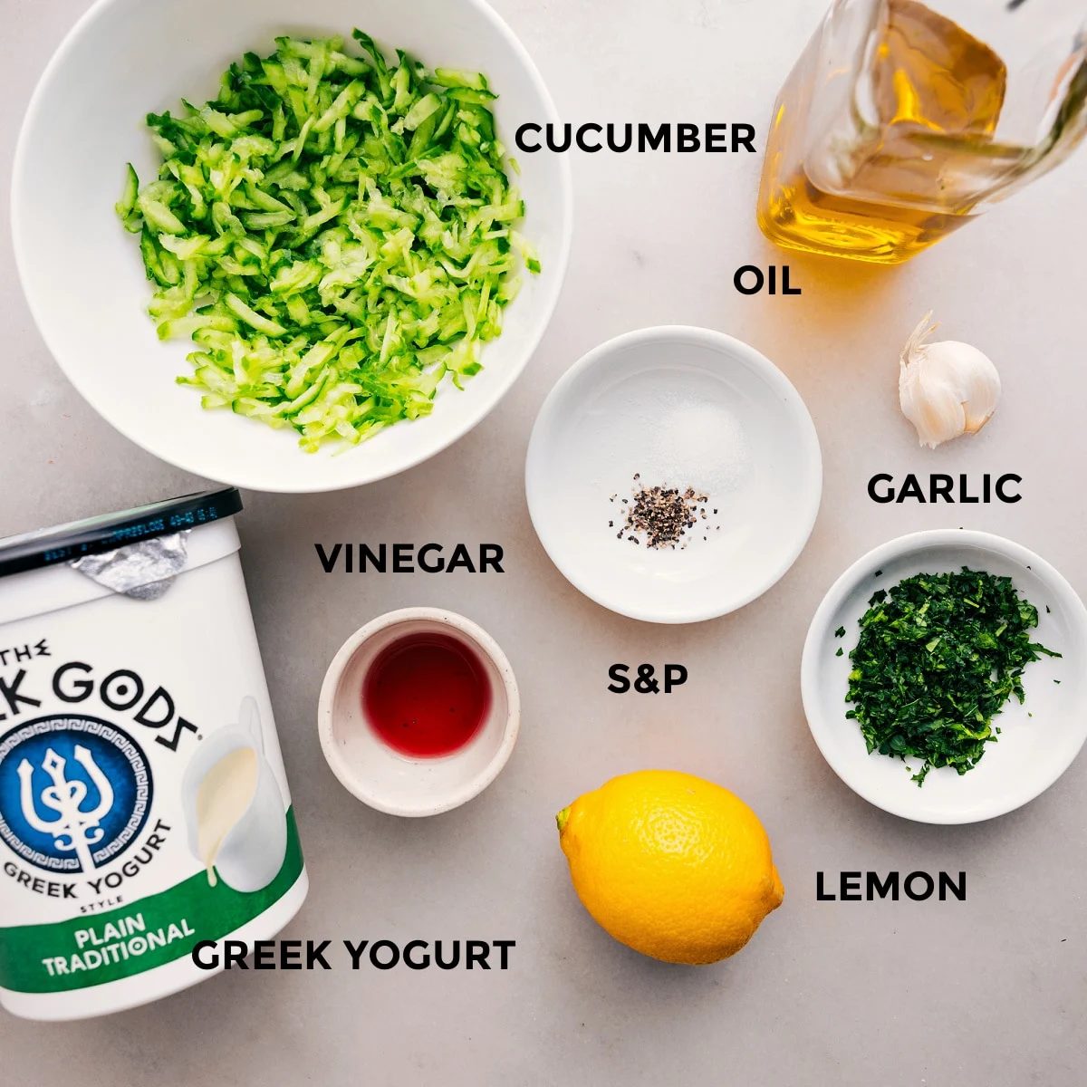 All the ingredients are prepped for straightforward assembly, including oil, cucumbers, yogurt, vinegar, garlic, herbs, salt, and pepper.