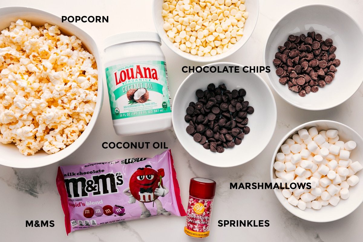 All the ingredients in this recipe prepped out for straightforward assembly including the popcorn, coconut oil, chocolate chips, marshmallows, M&Ms, and sprinkles.