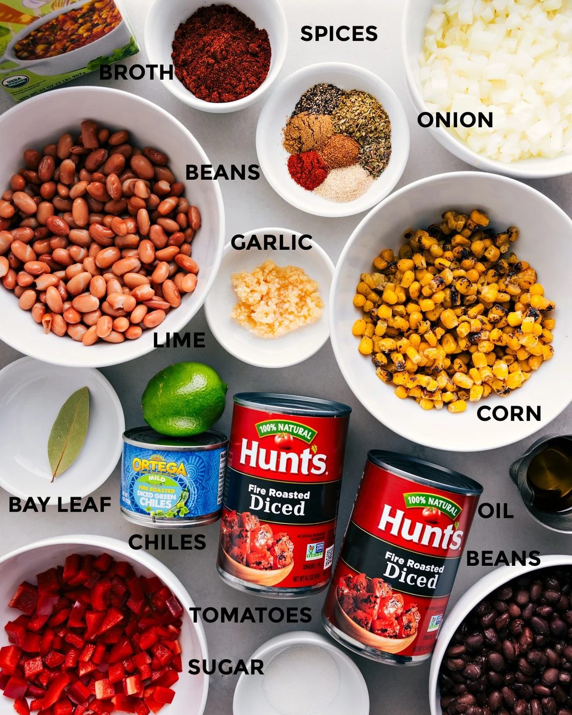 All the ingredients are prepped and ready for straightforward assembly—spices, veggies, beans, garlic, lime, broth, tomatoes, chiles, oil, and a bay leaf.