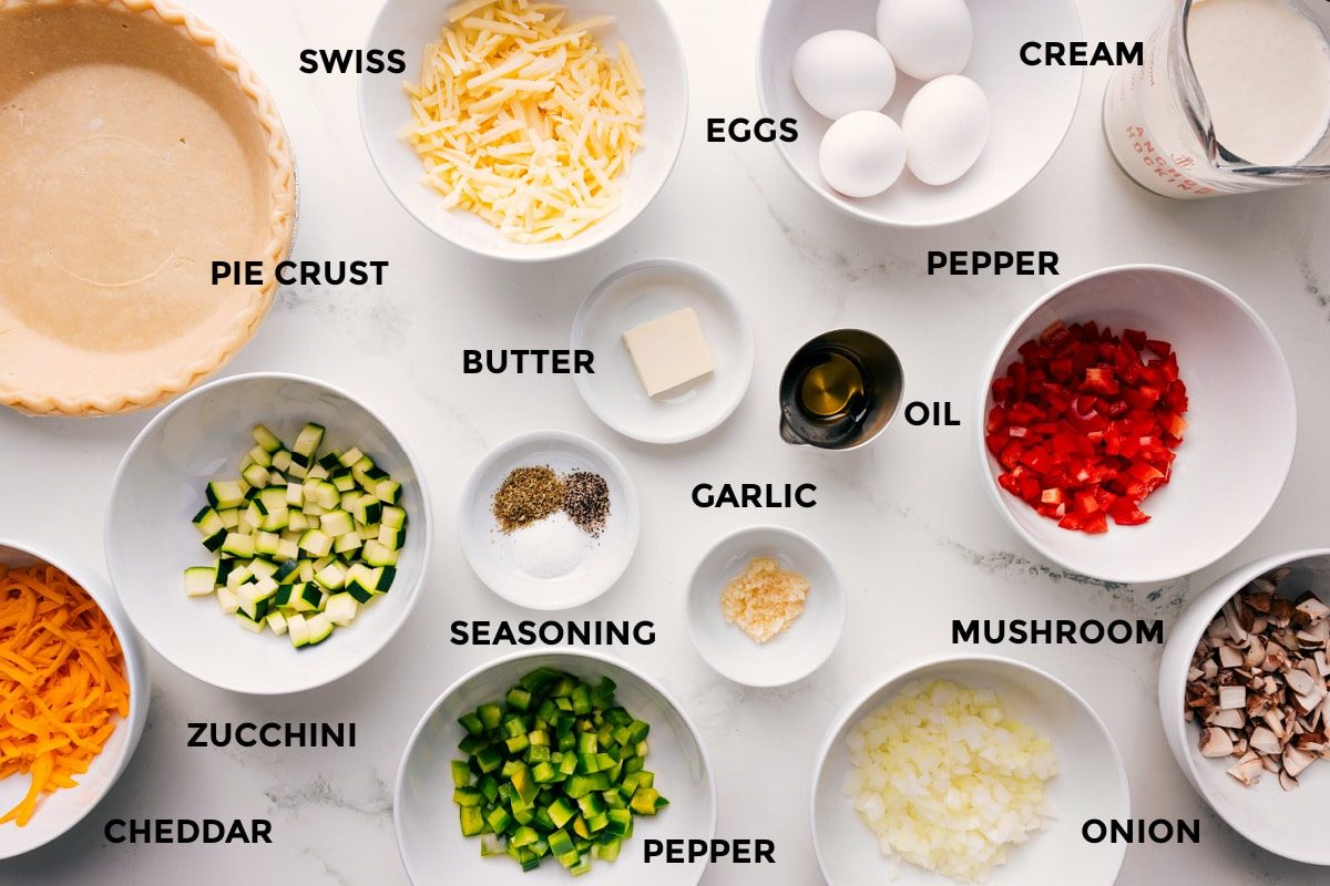 All the ingredients prepped and ready, including the pie crusts, cheese, zucchini, butter, seasonings, garlic, oil, onion, mushrooms, peppers, cream, and eggs.