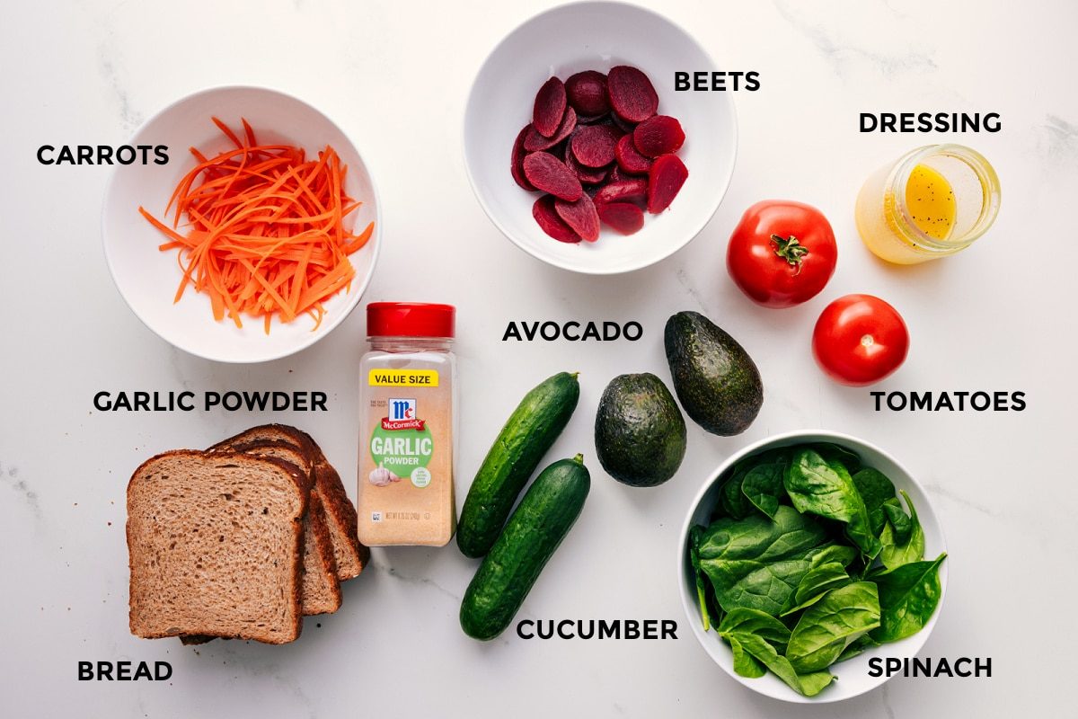 All the ingredients in this recipe prepped out for straightforward assembly including the carrots, garlic powder, bread, beets, avocado, cucumber, spinach, tomatoes, and dressing.