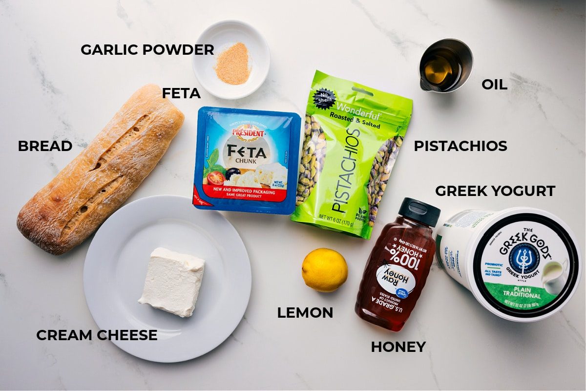 All the ingredients in this recipe prepped out for straightforward assembly including the bread, feta, cheese, pistachios, lemon, honey, yogurt, pistachios, and oil.