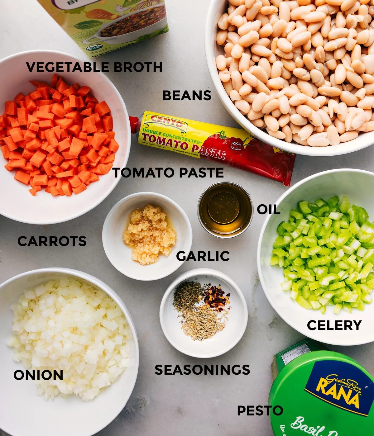 All the ingredients for this recipe are prepped and ready for straightforward assembly, including broth, beans, paste, oil, garlic, veggies, seasonings, and pesto.