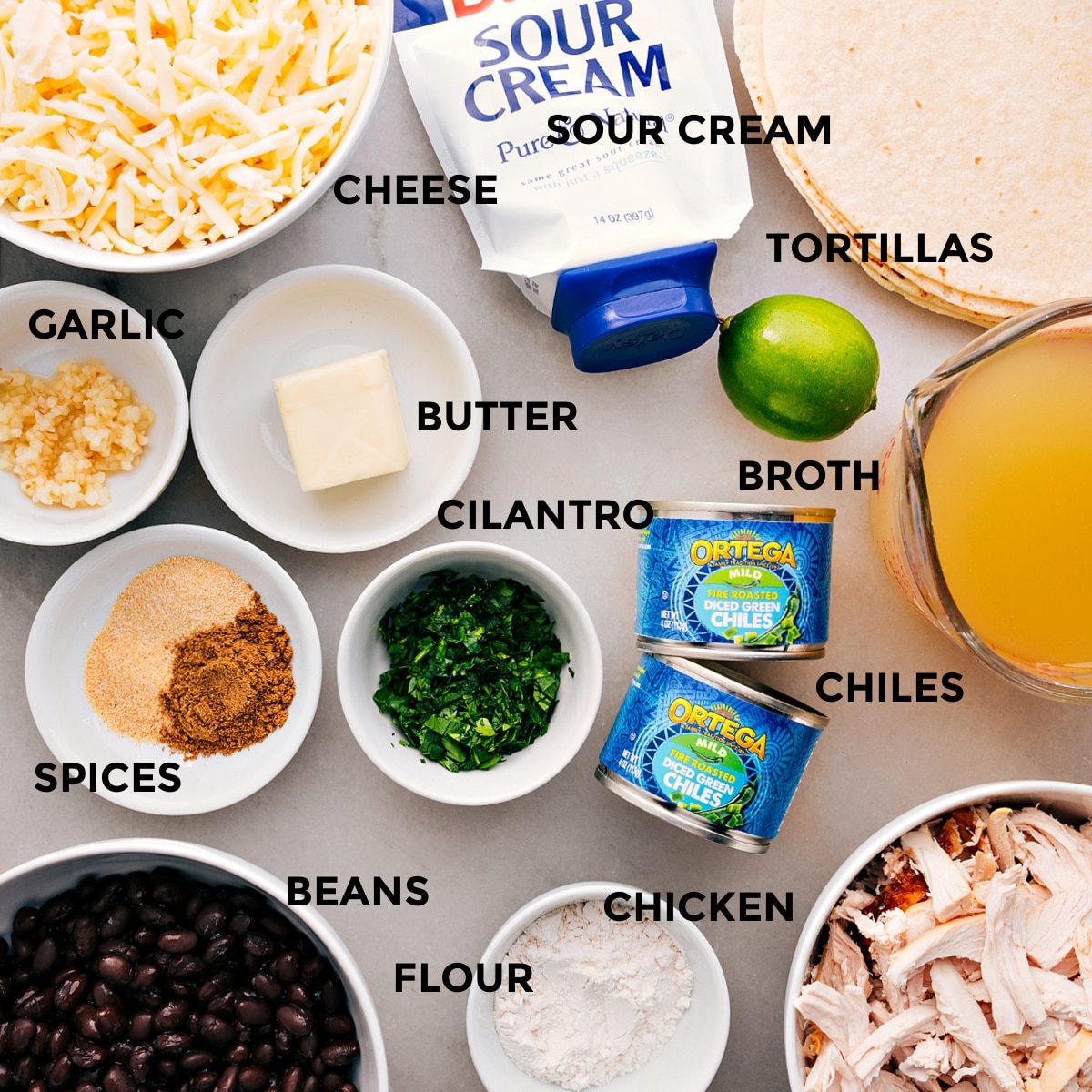 All the ingredients prepped and ready for straightforward assembly—cheese, tortillas, sour cream, broth, butter, cilantro, green chiles, garlic, spices, beans, chicken, and flour.