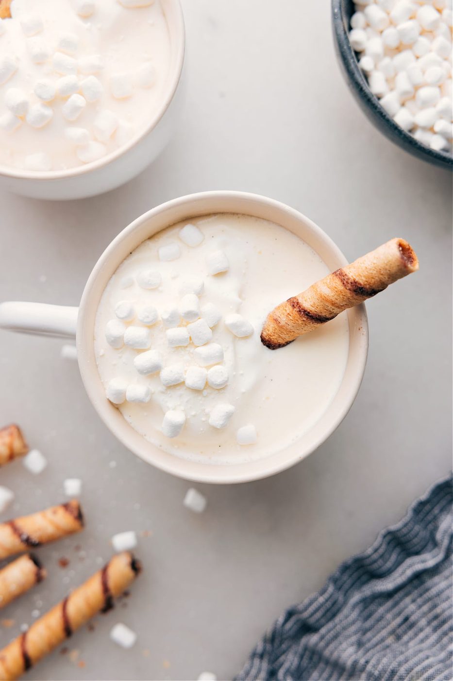 A mug of warm and satisfying White Hot Chocolate, with marshmallows floating on top and a chocolate straw coming out of it.