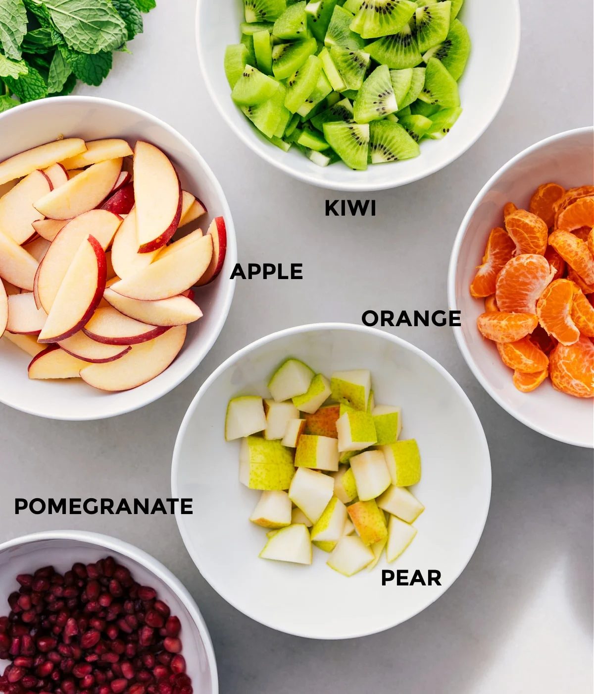 All the ingredients for this dish are prepped for straightforward assembly: kiwis, apples, oranges, pears, and pomegranates.