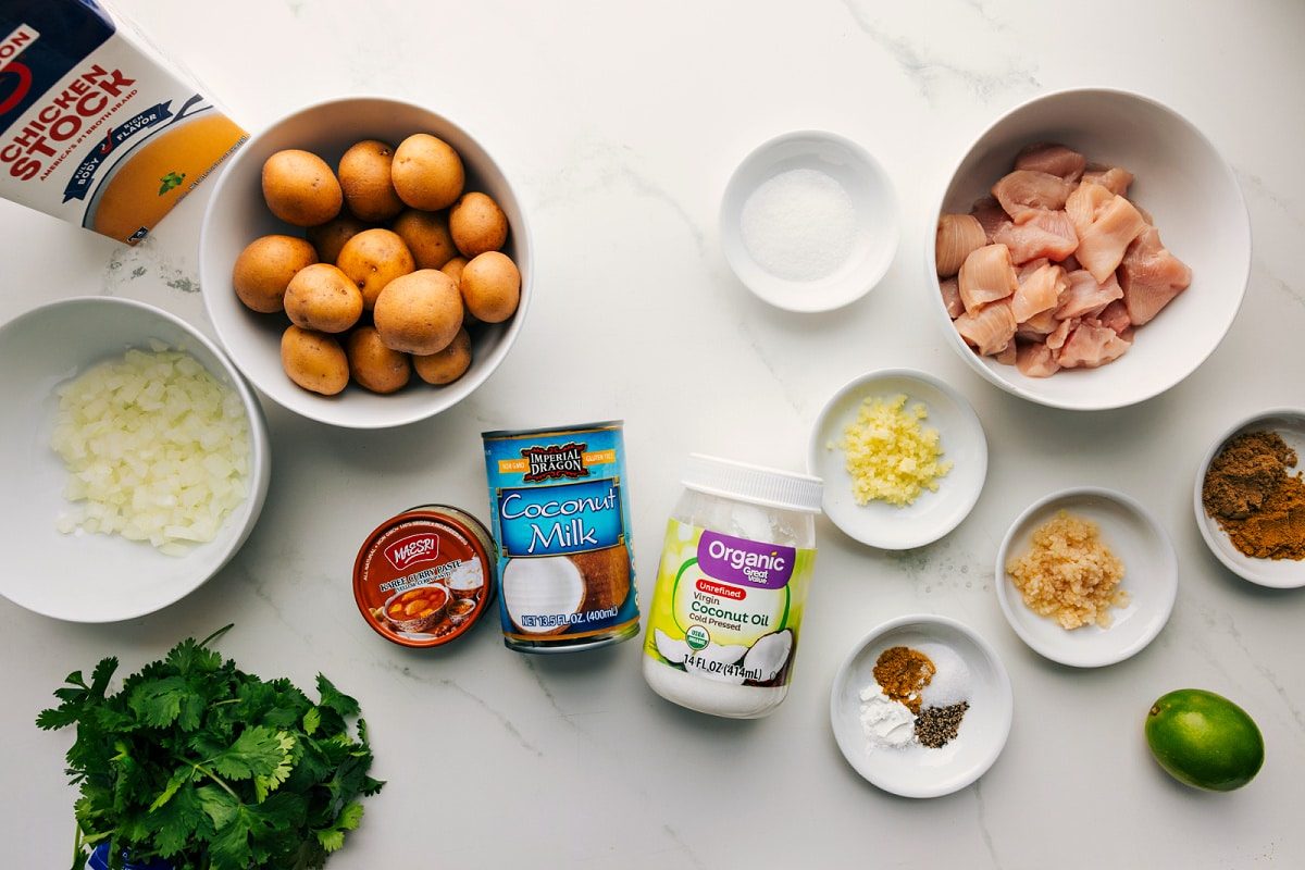 All the ingredients in this recipe prepped out for straightforward assembly including the stock, onions, cilantro, curry paste, coconut milk, coconut oil, spices, garlic, ginger, lime, chicken, potatoes, and sugar.