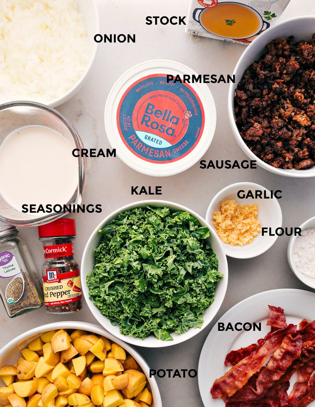 This recipe has all the ingredients prepped for straightforward assembly: stock, onion, Parmesan, sausage, cream, kale, garlic, flour, seasonings, bacon, and potatoes.