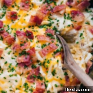 A warm, hearty scoop of crockpot hashbrown casserole, steaming and ready to be served, topped with fresh chives and crispy bacon.