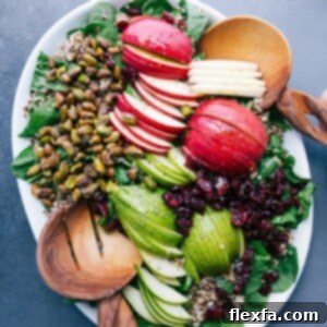 Quinoa apple salad on a platter with fresh greens, sliced apples, nuts, and more.