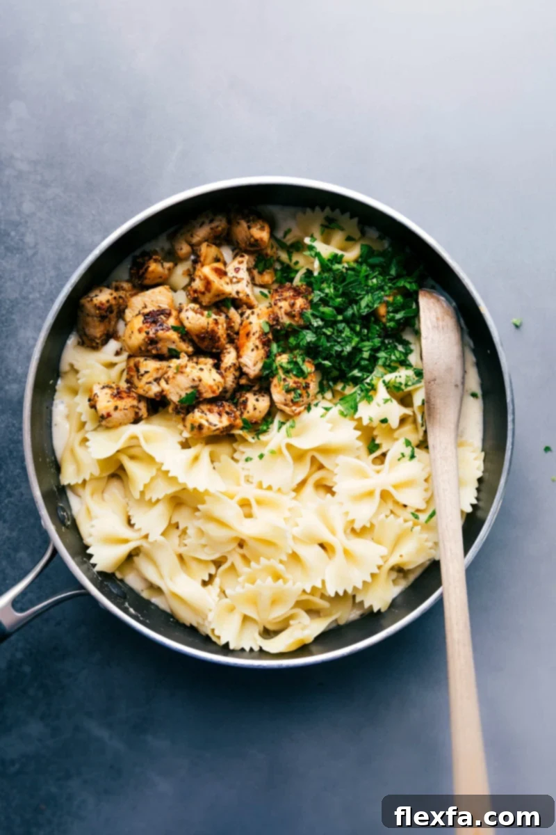 Cooked bowtie pasta, seasoned chicken, and freshly chopped parsley, waiting to be tossed together with the creamy lightened alfredo sauce to create a complete meal.