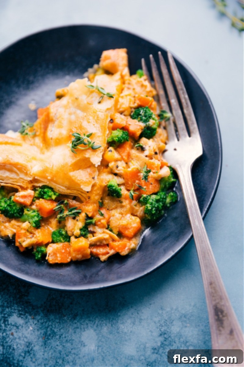 Our favorite Broccoli Cheddar Pot Pie: cheesy broccoli, seasoned chicken, and tender carrots with a buttery, flaky puff pastry crust. #dinner #quick #easy #simple #comfortfood #best #kidfriendly #familyfriendly #broccoli #cheddar #potpie An inviting, up-close overhead image of a slice of Broccoli Cheddar Pot Pie on a white plate, ready to be eaten, showcasing the rich filling and flaky crust.