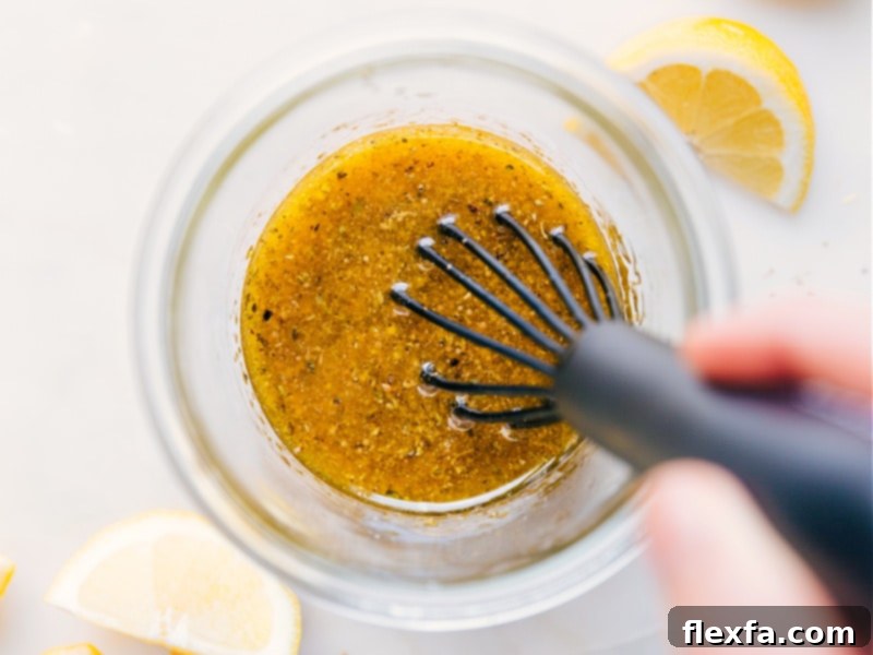 A clear glass jar filled with perfectly mixed Greek Salad Dressing, showcasing its beautiful golden hue and vibrant texture, ready to be poured generously over a fresh salad.