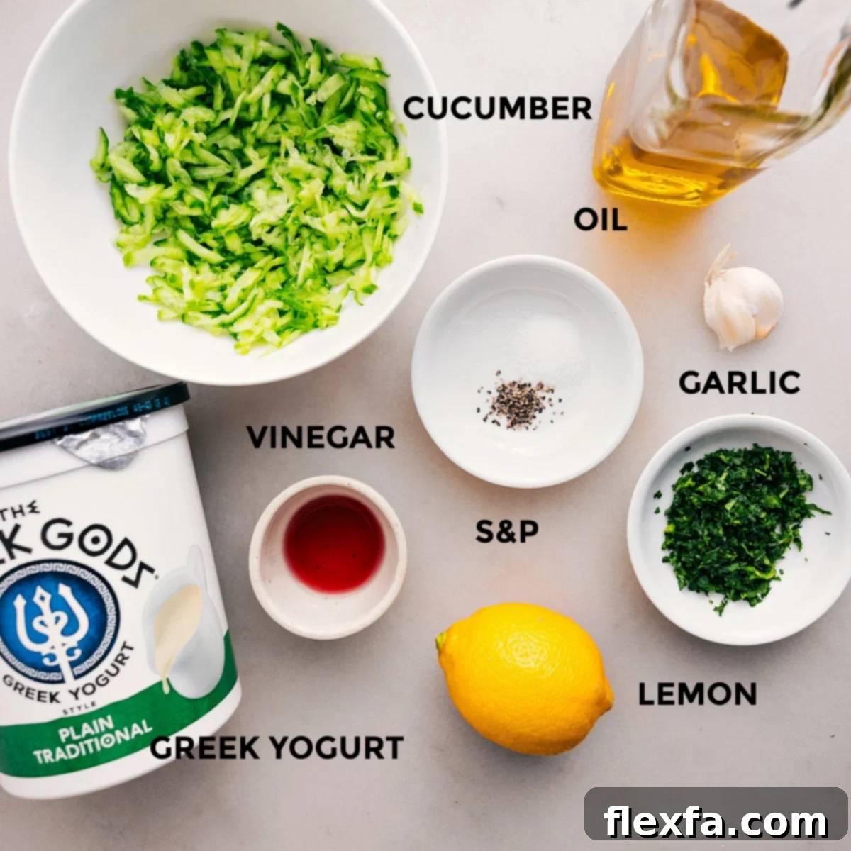All the fresh ingredients for Tzatziki Sauce laid out: Greek yogurt, English cucumbers, lemons, garlic, fresh dill, olive oil, red wine vinegar, salt, and pepper.