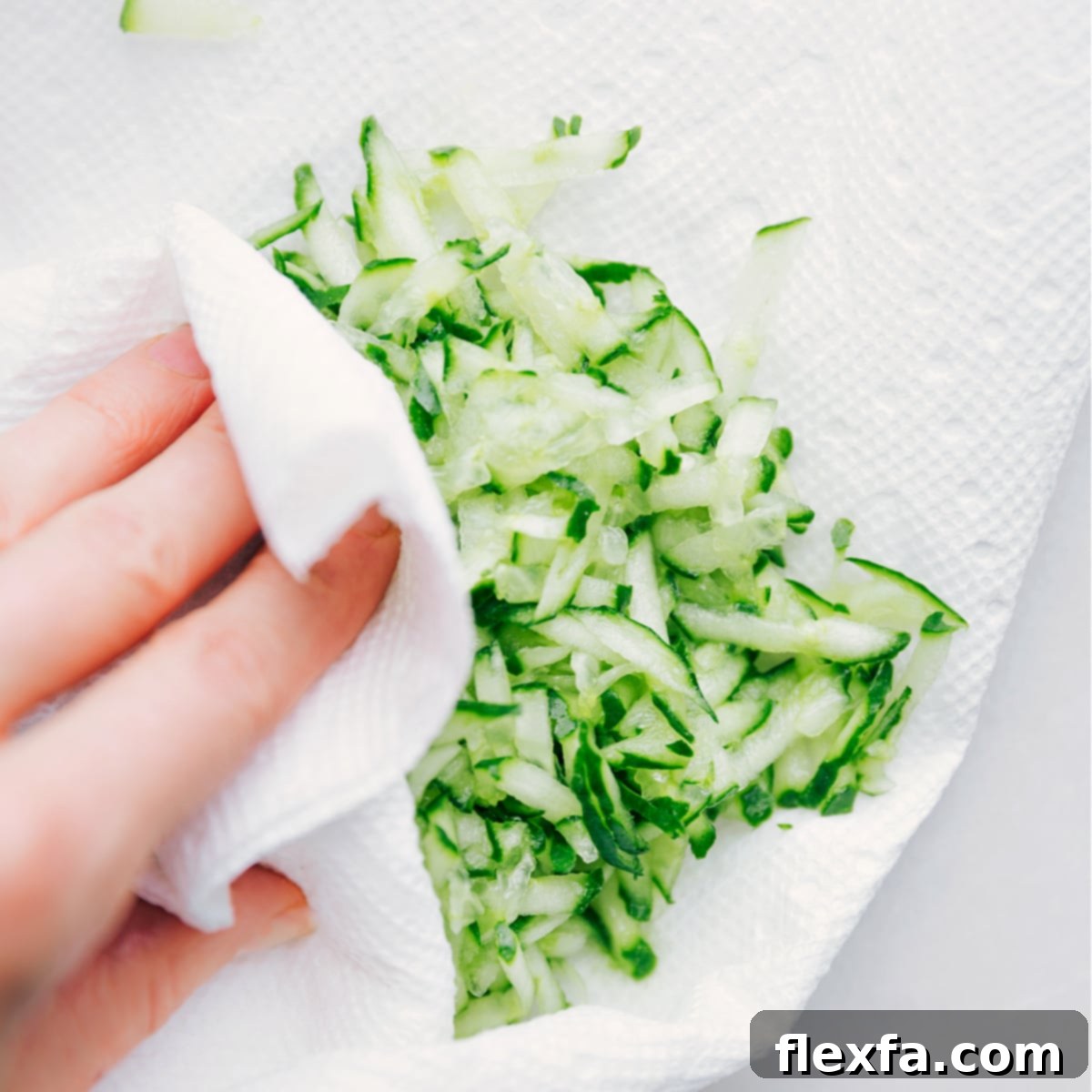 A person pressing grated cucumber with paper towels to extract excess liquid, a crucial step for thick Tzatziki Sauce.