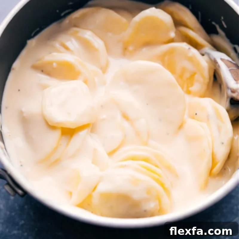 Crockpot Au Gratin Potatoes, close-up in the pot, perfectly cooked and waiting for garnish. Thinly sliced potatoes in an ultra-cheesy cream sauce are slow cooked to tender perfection. Save that precious oven space during the holidays OR prepare these in the summer while keeping the oven off and the heat out of the kitchen! Recipe via chelseasmessyapron #dinner #quick #easy #simple #healthy #best #thanksgiving #familyfriendly #crockpot #augratin #potatoes Up-close overhead image of the Crockpot Au Gratin Potatoes in the slow cooker, ready for the final touches