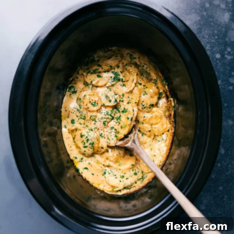 Delicious Crockpot Au Gratin Potatoes ready to be served! Perfect for saving precious oven space during the holidays or keeping your kitchen cool in the summer. The slow cooker is a lifesaver for either scenario! Recipe via chelseasmessyapron #dinner #quick #easy #simple #healthy #best #thanksgiving #familyfriendly #crockpot #augratin #potatoes Overhead image of the Crockpot Au Gratin Potatoes ready to be enjoyed with a spoon