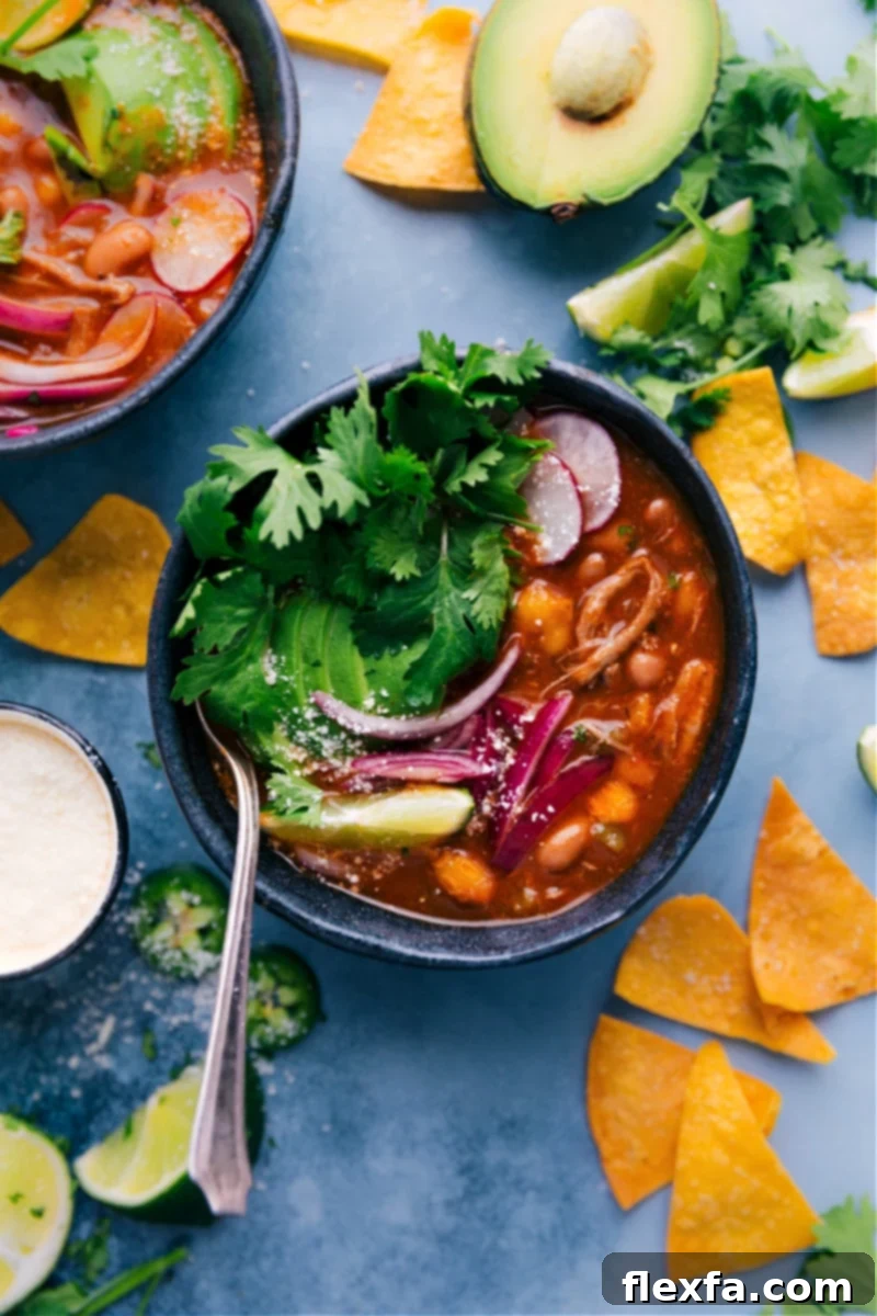 Try this quick 30-minute Mexican-inspired recipe, Pozole, complete with hominy, pulled pork, and loads of delicious toppings! While an authentic pozole can take several hours to make, this recipe can be on the table in 30 minutes or less! Recipe via ChelseasMessyApron #dinner #quick #easy #simple #best #clean #mexican #tortilla #beans #avocado #cilantro #lime #pozole Overhead image of Quick Pozole in a bowl with fresh toppings like cilantro, lime, and avocado.