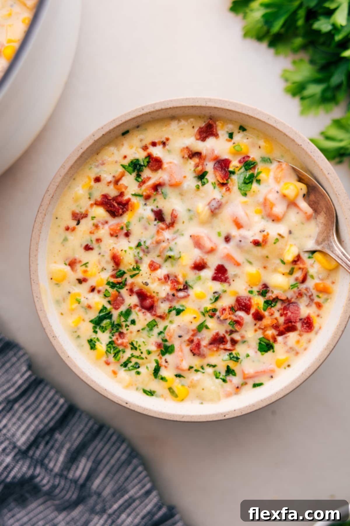 Corn chowder topped with crumbled bacon and fresh parsley in a bowl, showcasing its rich, creamy texture and vibrant ingredients.