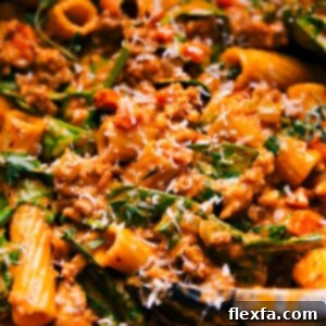 Close-up of a serving of Creamy Sausage Rigatoni in a white bowl, garnished with fresh herbs and grated Parmesan.