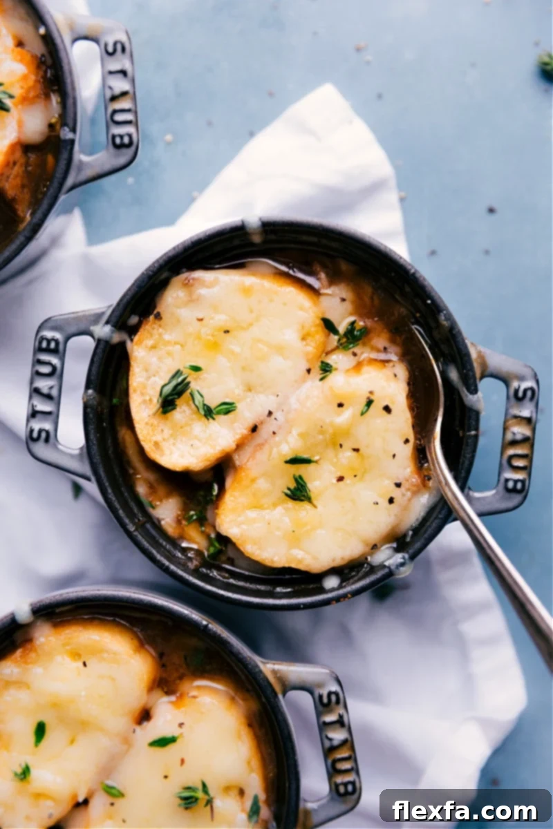 A steaming bowl of homemade French Onion Soup, topped with golden-brown Gruyere cheese and a toasted crouton, served on a rustic wooden surface.