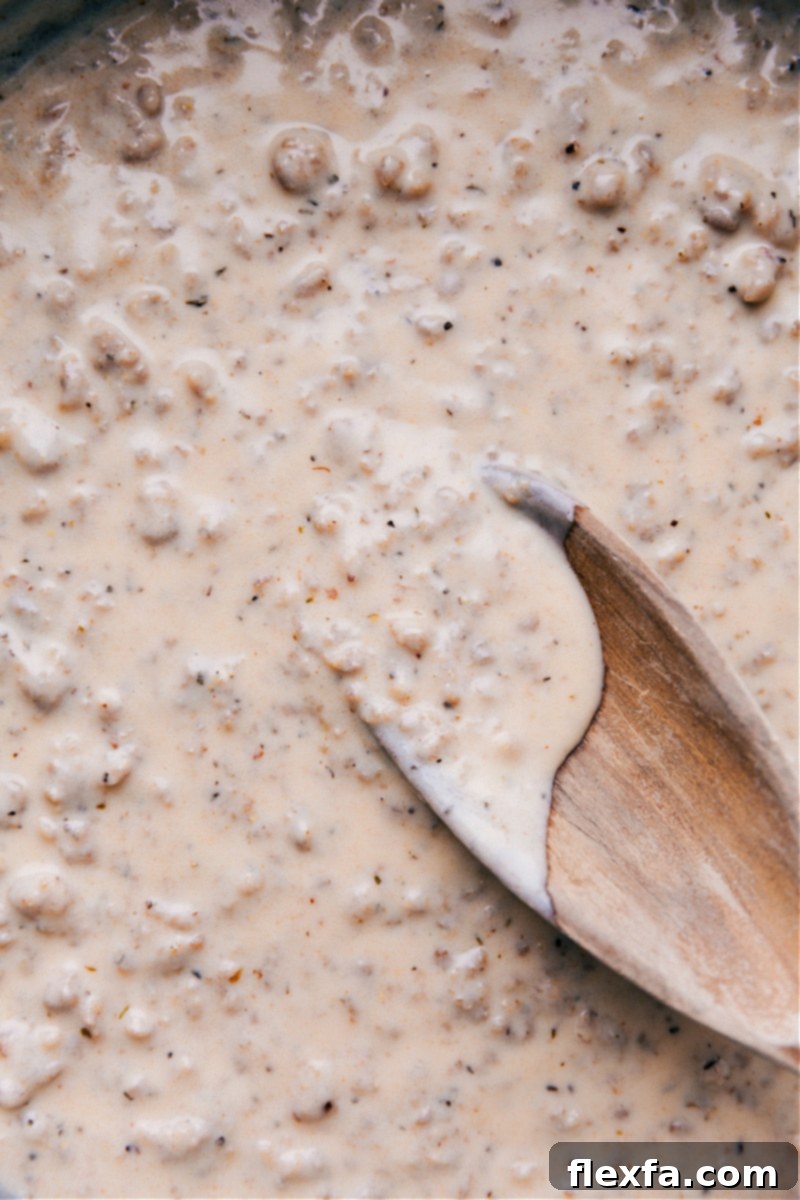 Overhead view of rich, creamy sausage gravy simmering in a large pan, ready to be served over warm biscuits.