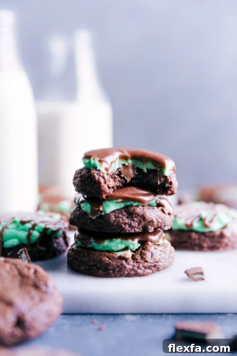 Stack of three fudgy Mint Brownie Cookies, with the top cookie having a bite taken out, revealing the soft interior, green mint frosting, and chocolate ganache drizzle.