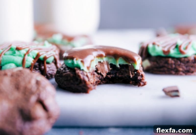 Close-up view of a freshly baked Mint Brownie Cookie, showing its fudgy texture, green peppermint frosting, and chocolate ganache drizzle.