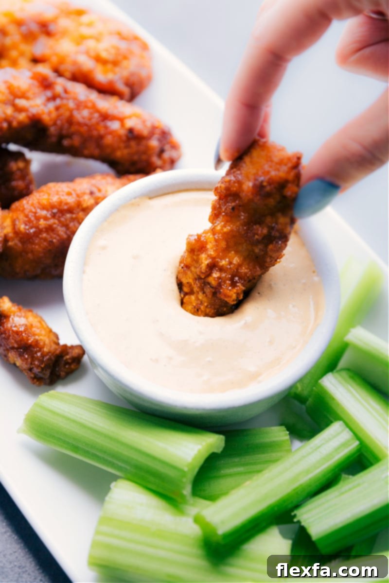Image of a piece of perfectly cooked chicken being dipped into the creamy Chipotle Ranch Dip, highlighting its appealing texture.
