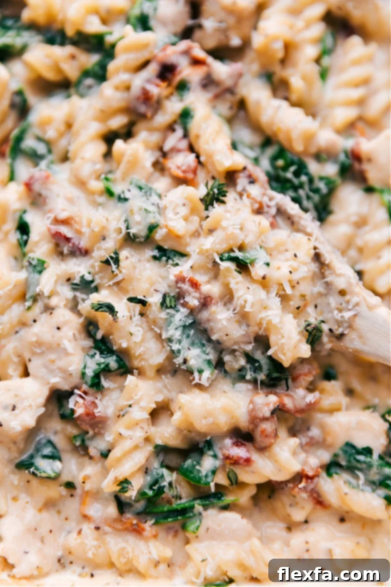 This is our favorite Tuscan Chicken Pasta -- it's loaded with flavor and made all in ONE pan. That's right -- uncooked chicken, uncooked pasta, and uncooked veggies all get tossed together and baked to creamy and cheesy perfection! Recipe via ChelseasMessyApron #dinner #quick #easy #simple #best #spinach #tomatoes #tuscan #chicken #pasta Overhead view of a beautiful, creamy Tuscan Chicken Pasta, loaded with chicken, spinach, and sun-dried tomatoes, served in a white casserole dish.