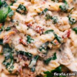 A vibrant close-up of the finished Tuscan Chicken Pasta in a serving bowl, highlighting the creamy sauce, tender chicken, and colorful vegetables.