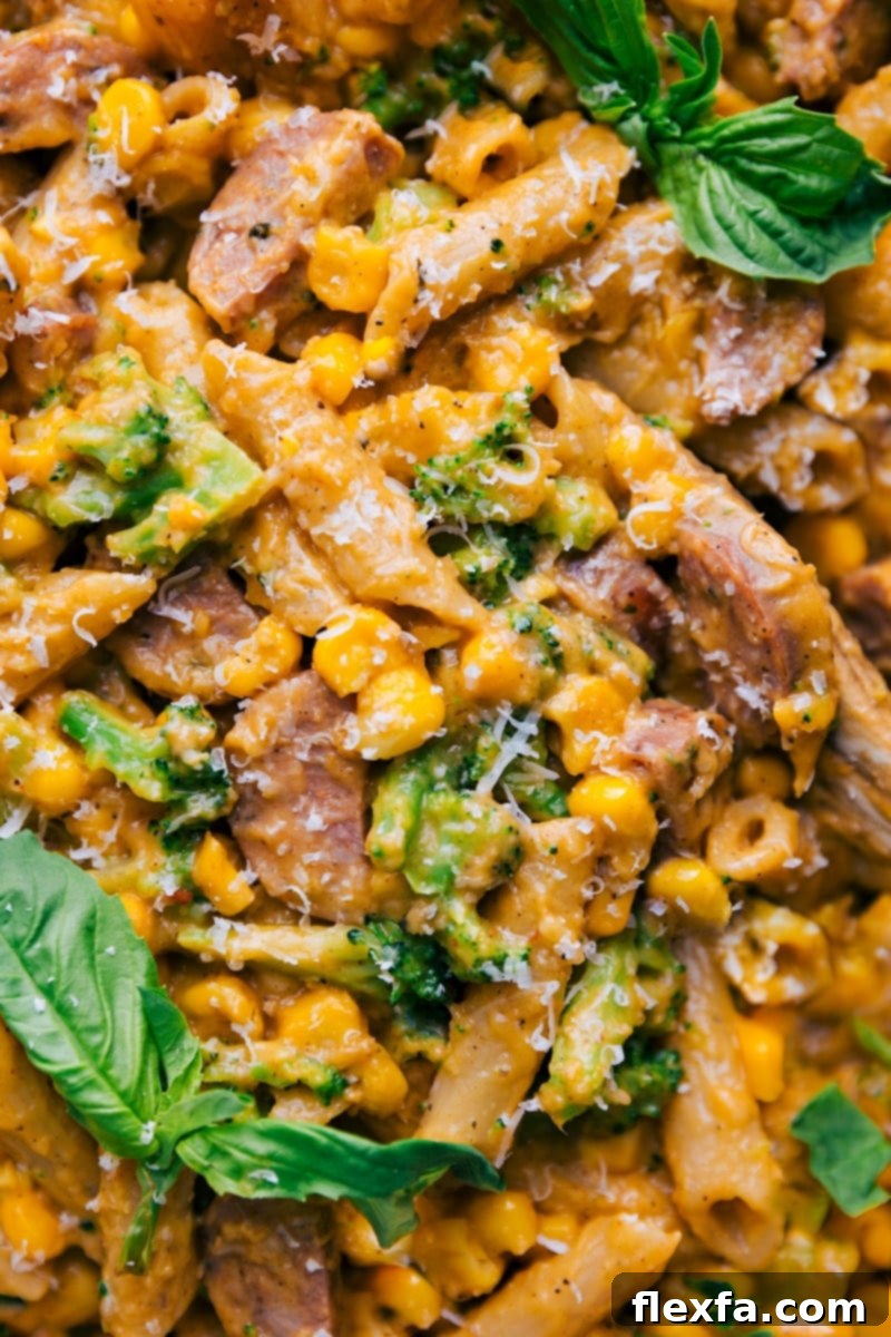 Overhead image of a Healthy Pasta Bake fresh from the oven, showcasing creamy texture, pasta, vibrant vegetables, and savory chicken sausage. A sprig of fresh basil garnishes the dish.
