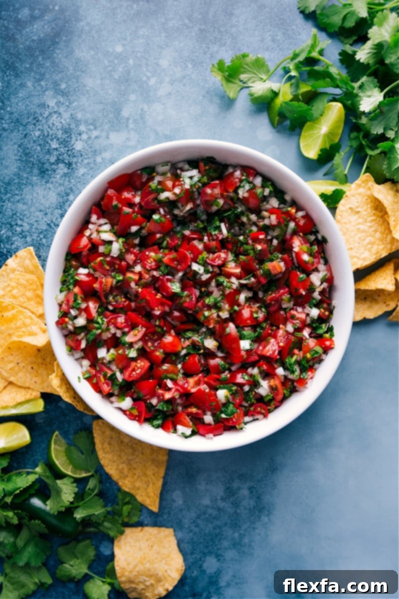 Overhead image of a beautifully arranged bowl of fresh Pico de Gallo, showcasing diced red tomatoes, white onions, green cilantro, and jalapeños.