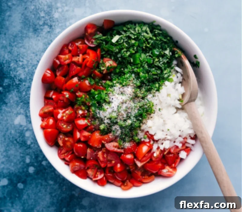 Close-up process shot of a hand sprinkling salt and freshly ground black pepper over a bowl of diced tomatoes, onions, and cilantro.