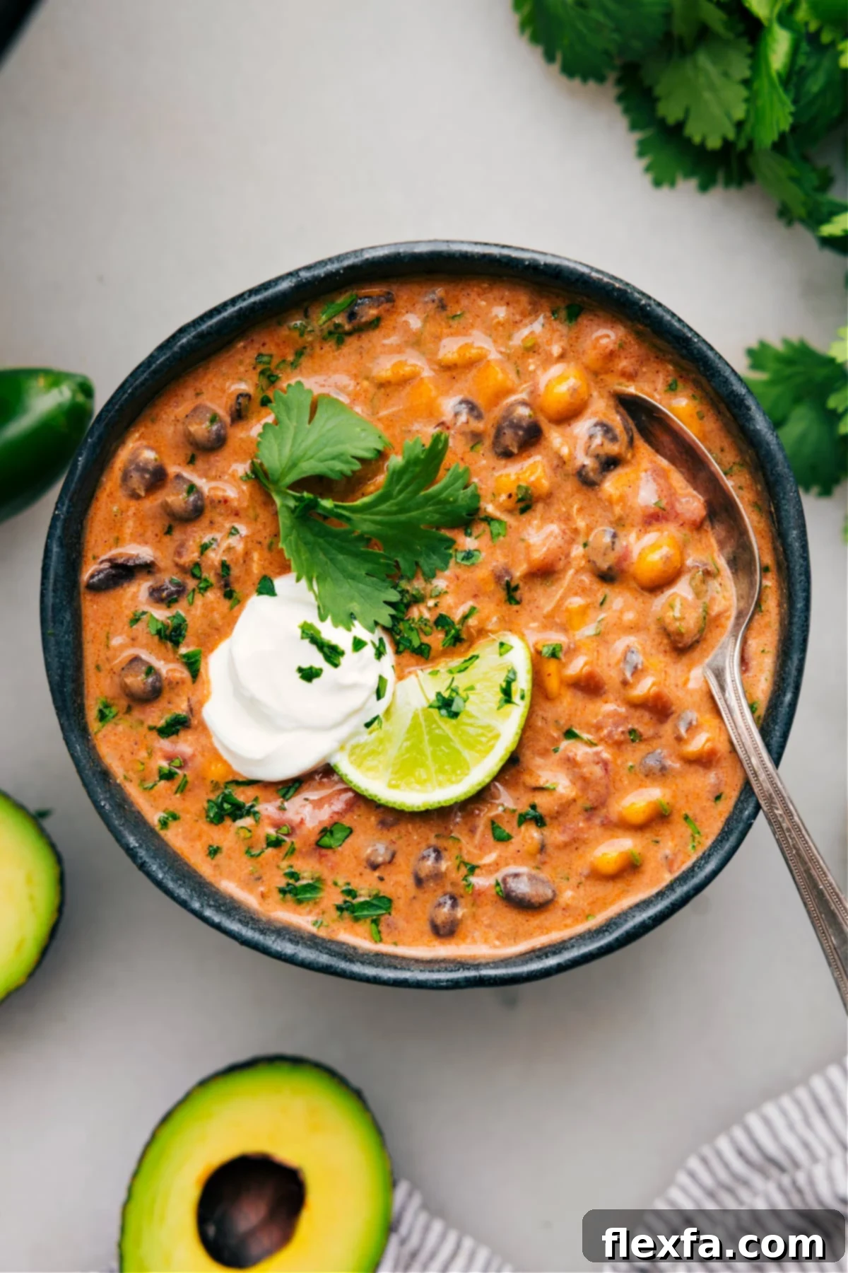 A big bowl of creamy chicken chili topped with fresh lime wedges, vibrant cilantro, and a dollop of cool sour cream, ready to enjoy. This is an easy dump-and-go crockpot chicken chili recipe.