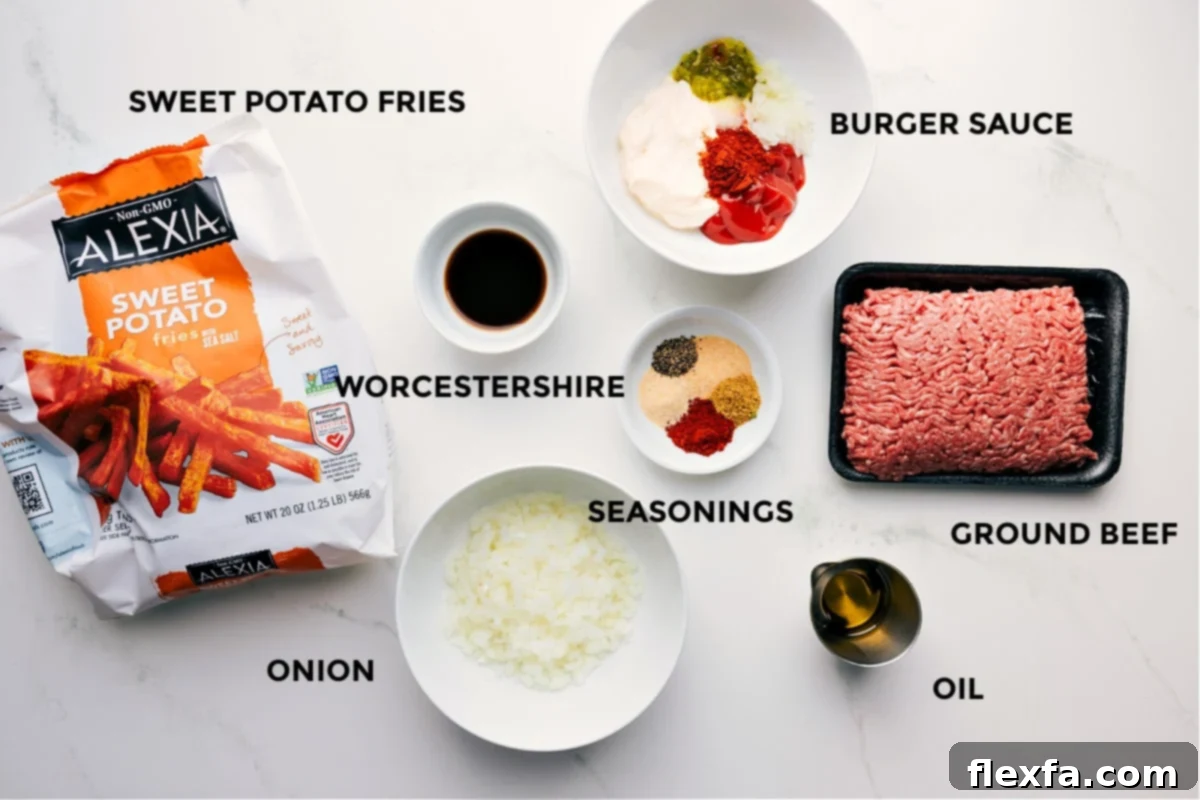 A comprehensive spread of prepped ingredients for the Burger Bowl recipe, including golden sweet potato fries, a bowl of homemade burger sauce, a bottle of Worcestershire sauce, various spices, raw ground beef, olive oil, and freshly chopped yellow onion.