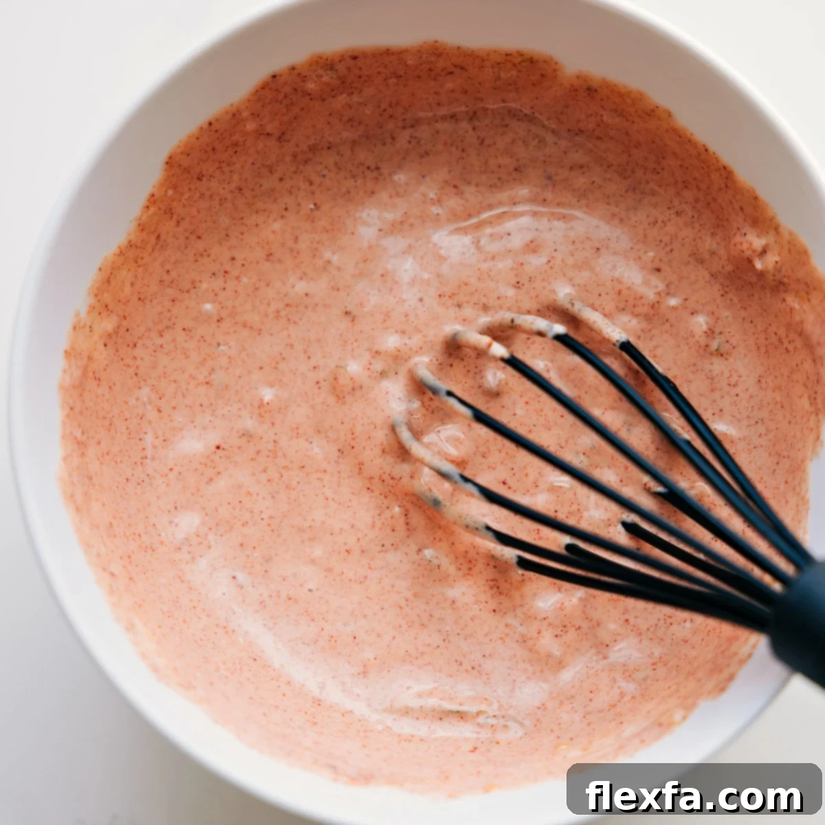 Homemade burger sauce being skillfully whisked in a glass bowl, showcasing its smooth, creamy, and inviting texture, perfectly ready to be drizzled over the Burger Bowls.