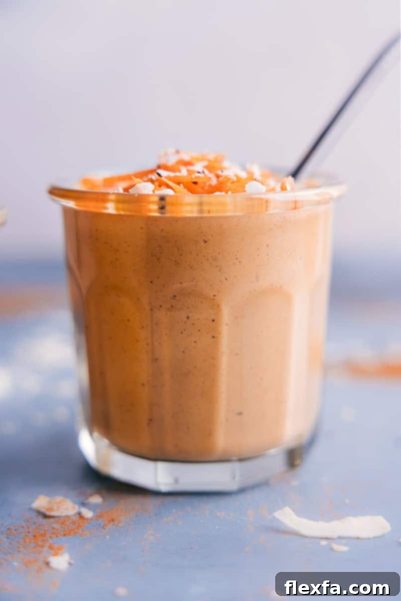 A tall glass of creamy Carrot Smoothie with a straw, ready for sipping, against a rustic background, highlighting its inviting color and texture.