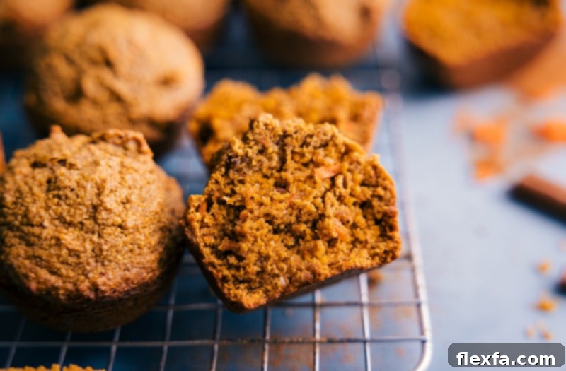A close-up image of two Healthy Carrot Muffins, one perfectly whole and the other cut in half to reveal its moist, spiced interior filled with grated carrots.