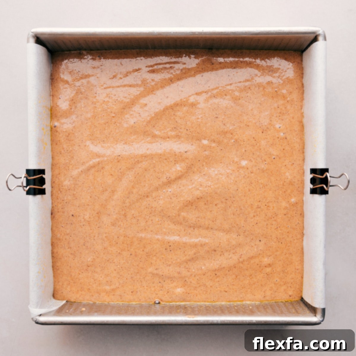 Pouring the smooth, healthy apple cake batter into a parchment-lined square baking pan before baking, showcasing the perfect consistency.