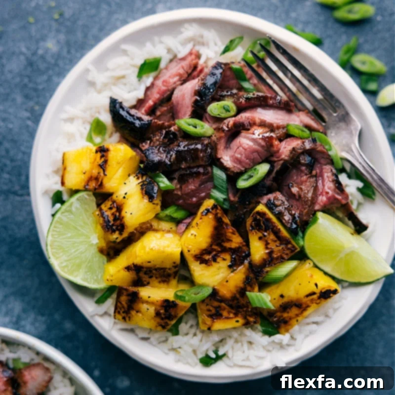 An inviting overhead view of a completed Grilled Pineapple Steak dinner, featuring slices of succulent flank steak, charred pineapple chunks, and a generous serving of fluffy coconut-lime rice, garnished with fresh green onions and lime wedges.