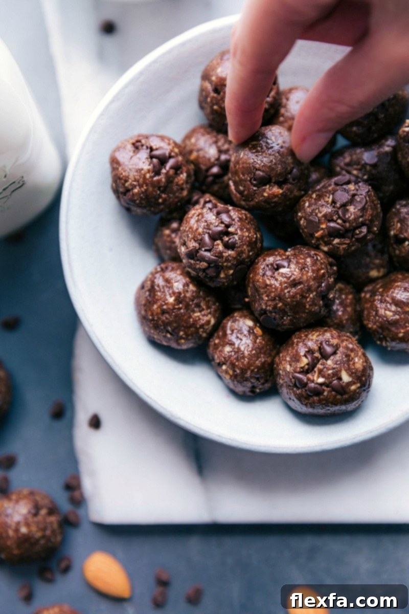 A hand rolling a portion of chocolate protein ball dough into a perfect sphere.