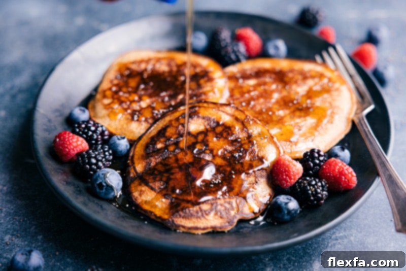 An appetizing image of healthy pancakes piled high, with rich maple syrup being poured over them, creating a glossy, enticing sheen, surrounded by fresh berries.