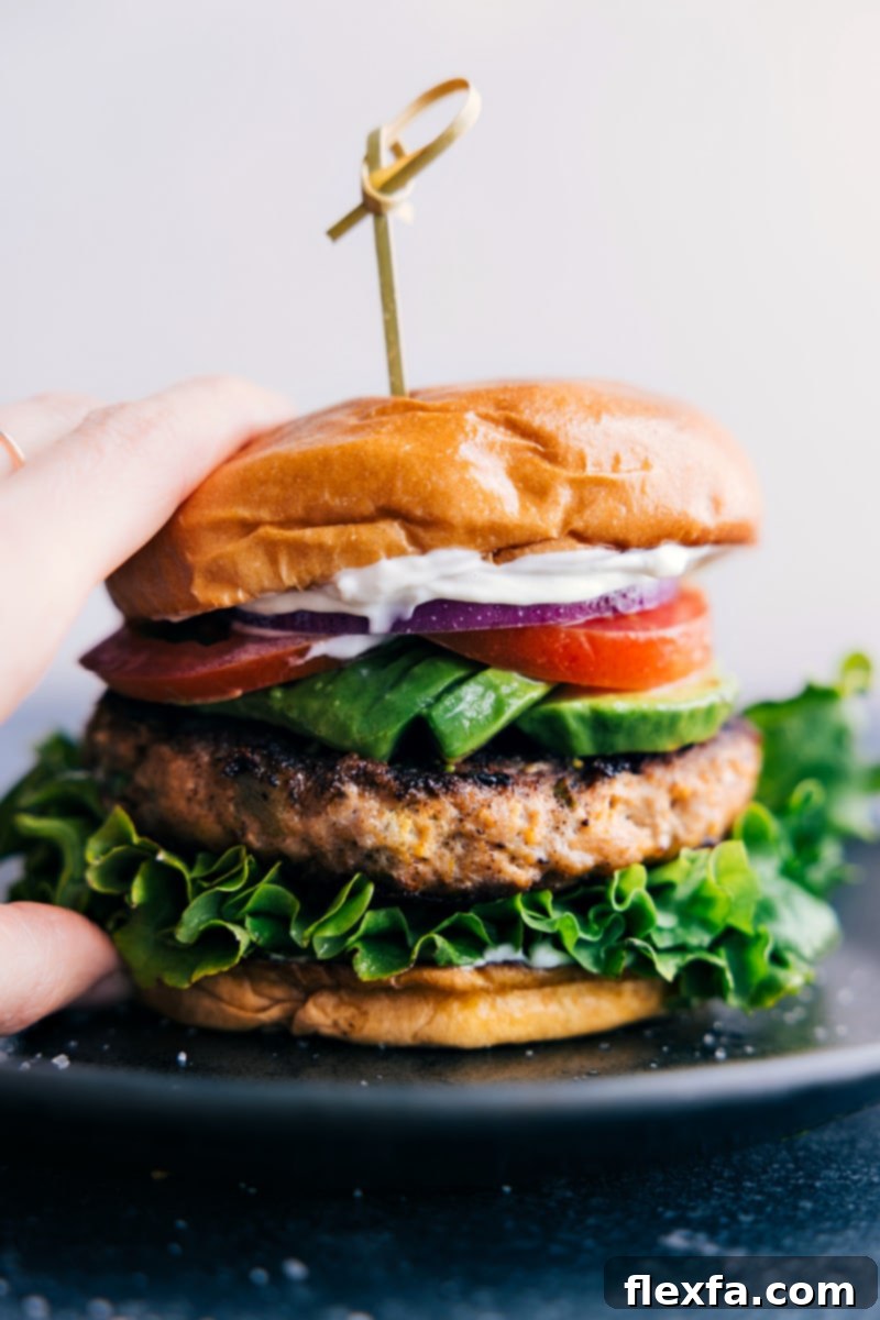 Close-up view of a perfectly assembled Green Chile Turkey Burger, stacked high with fresh toppings, a juicy patty, and a golden toasted bun