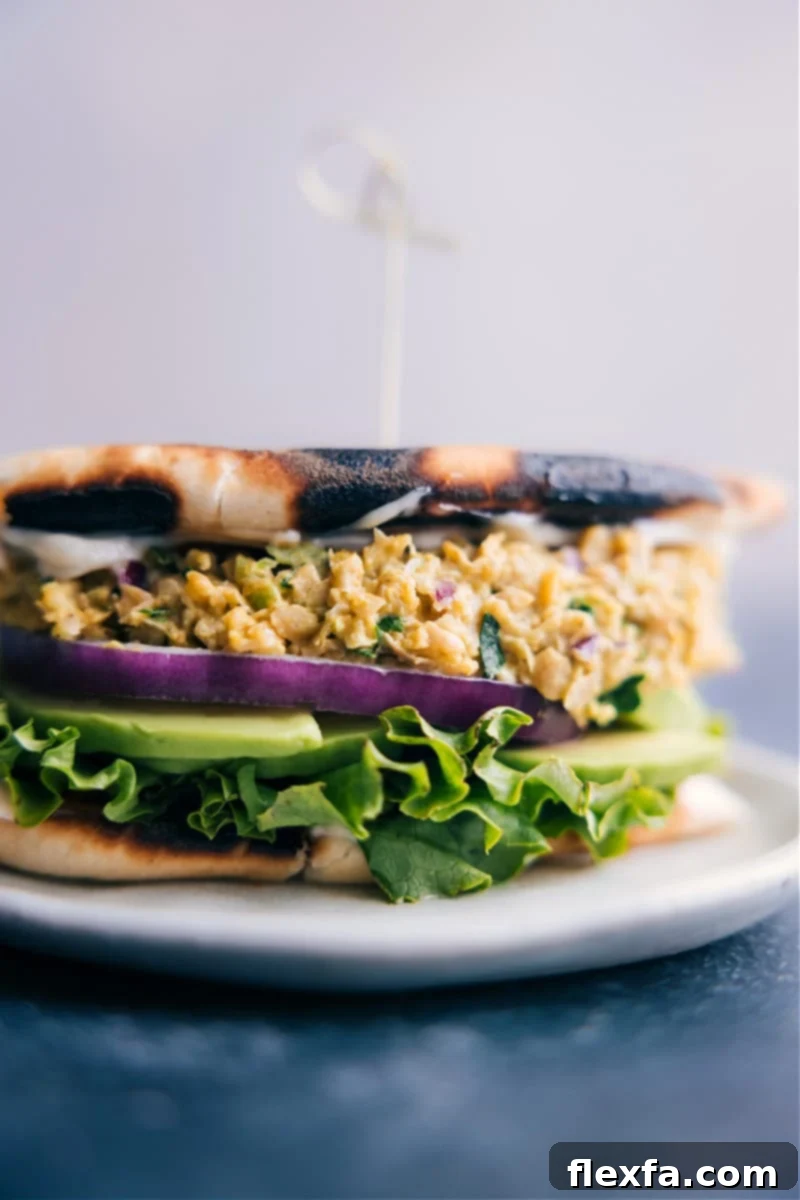 A beautifully plated Curried Chickpea Sandwich on whole-grain bread, surrounded by fresh greens.