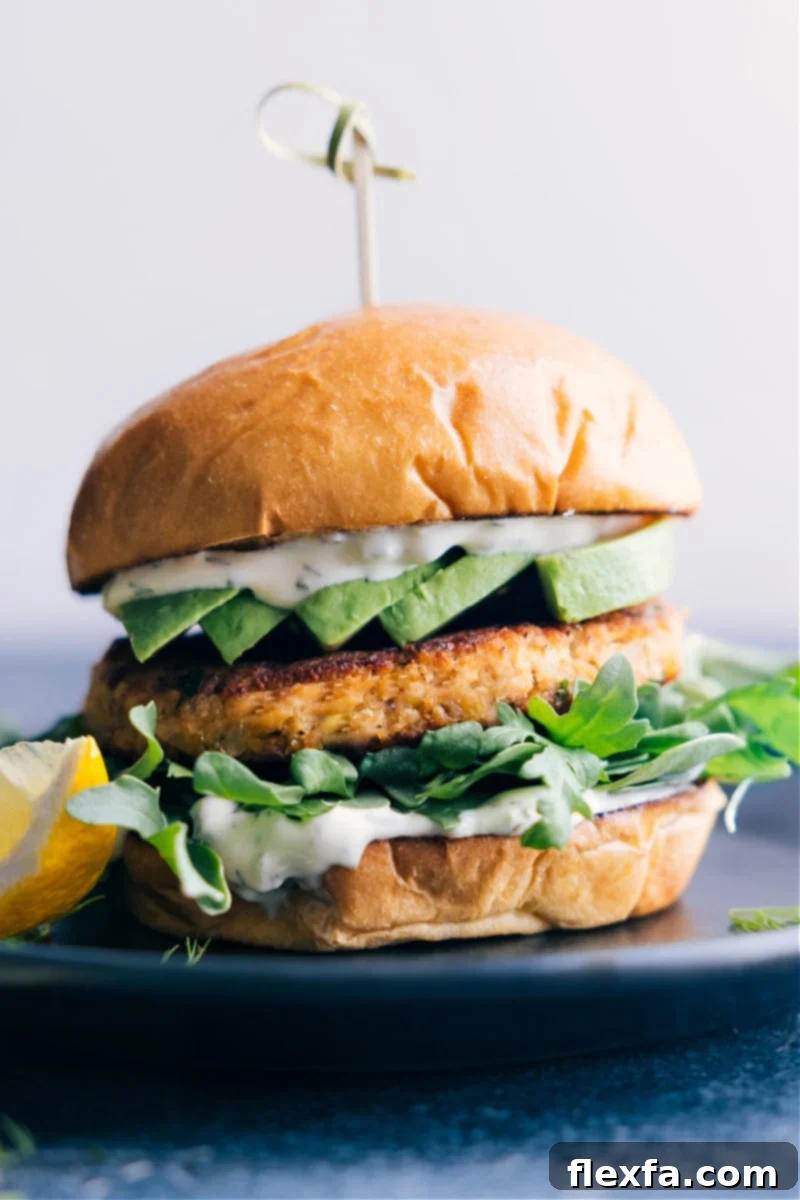 These are our all-time favorite Salmon Burgers complete with a buttered and toasted brioche bun, a succulent and well-seasoned salmon patty, and the best tartar sauce. Add a handful of greens and a ripe avocado to your burger and be ready to have these burgers on permanent dinner rotation! Recipe via ChelseasMessyApron #dinner #quick #easy #simple #familyfriendly #kidfriendly #grilled #healthy #cleaneating #salmon #burger A perfectly assembled Salmon Burger on a plate, featuring a golden-brown salmon patty, fresh greens, avocado slices, and creamy tartar sauce, all nestled in a toasted brioche bun.